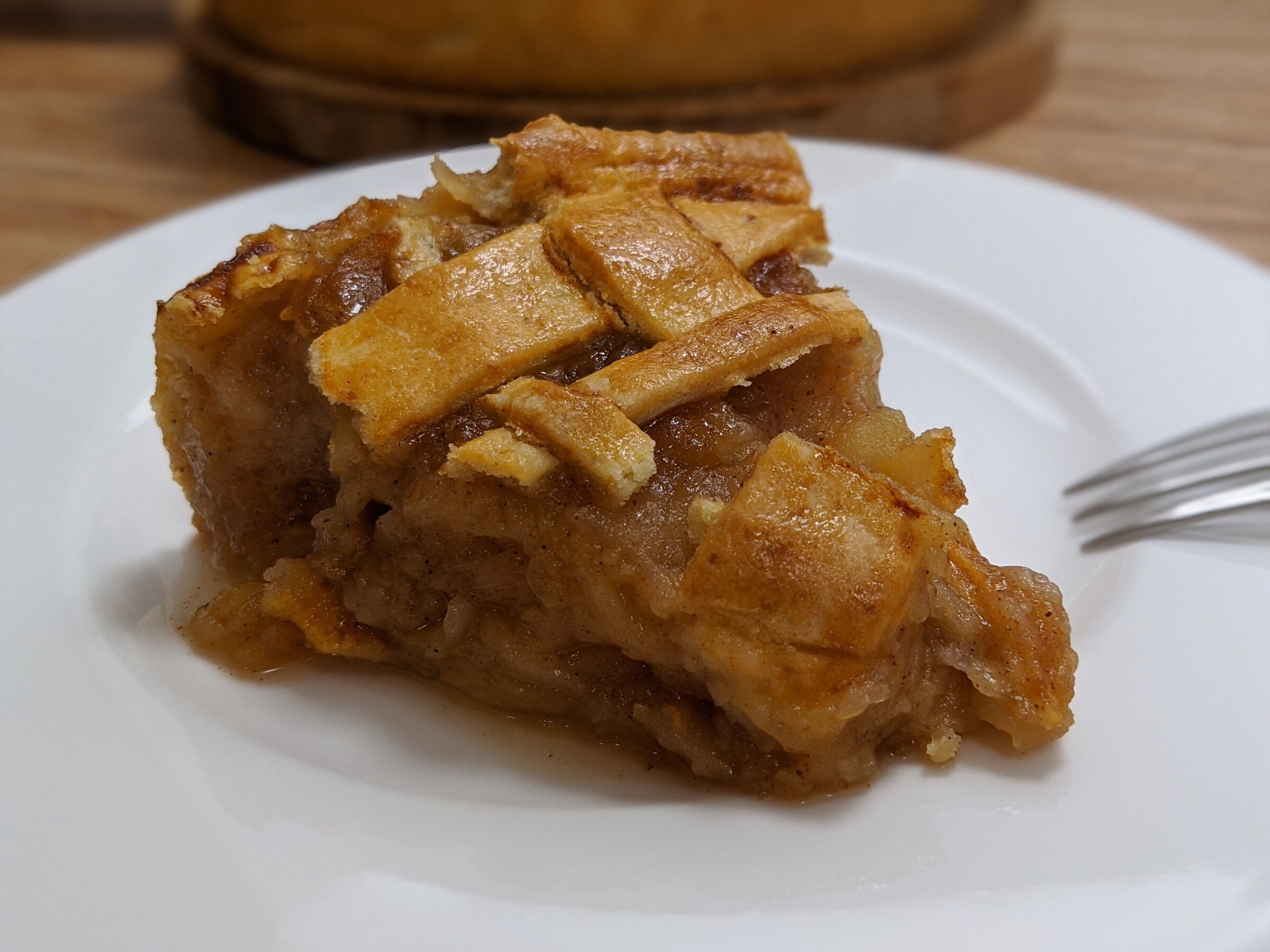 A slice of lattice-topped apple pie on a white plate with a fork