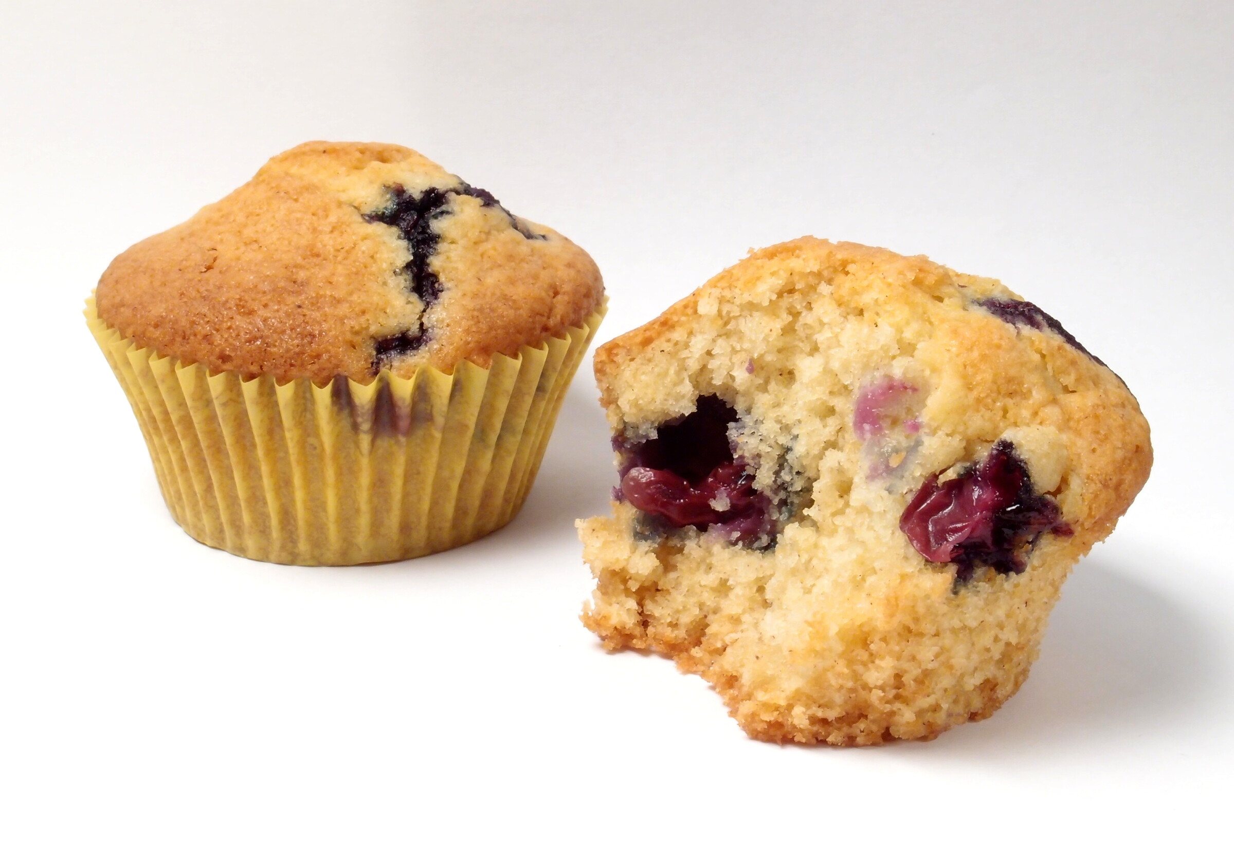 Two blueberry muffins, one broken open to show the blueberries inside