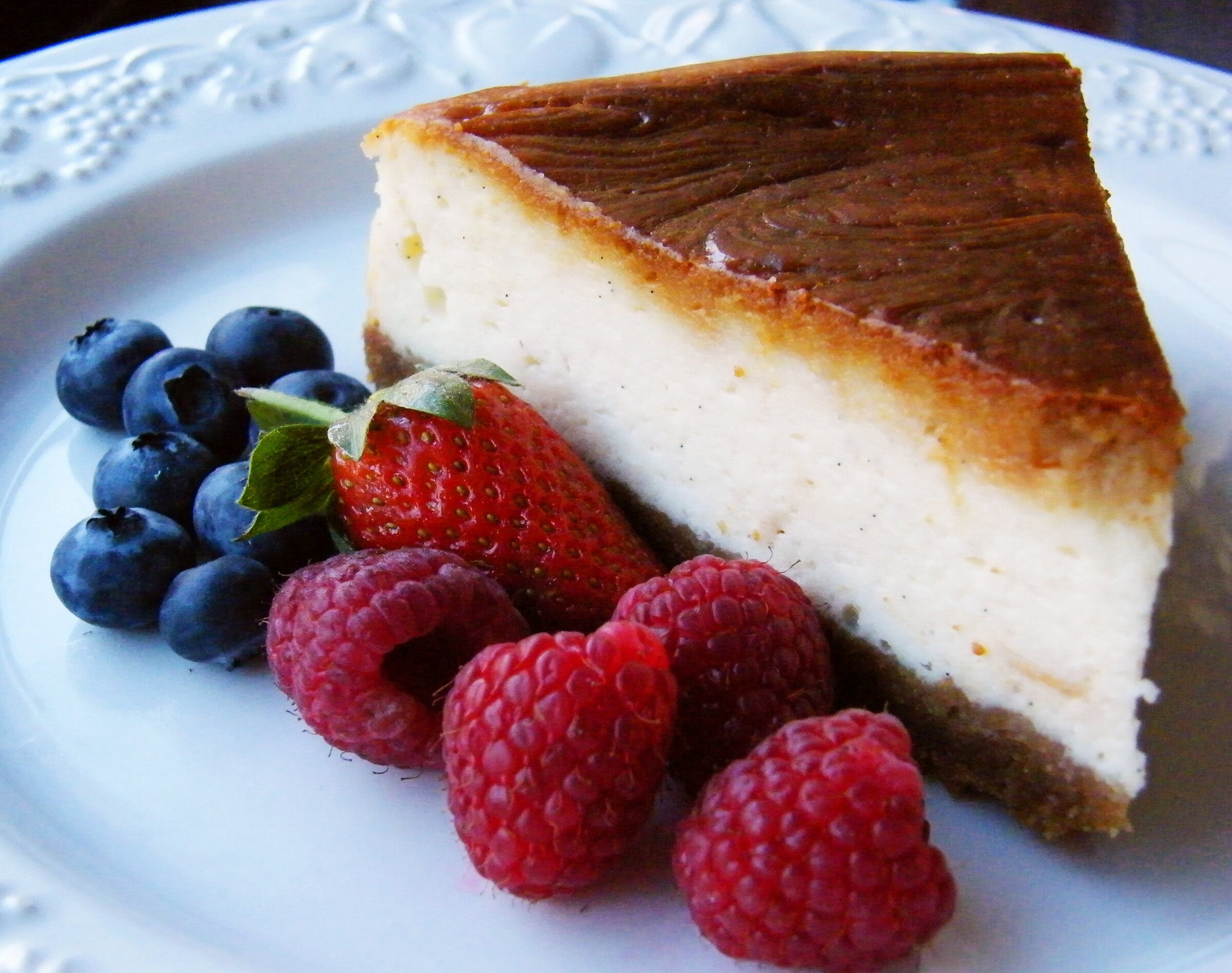 A slice of baked New York cheesecake with blueberries, strawberries and raspberries