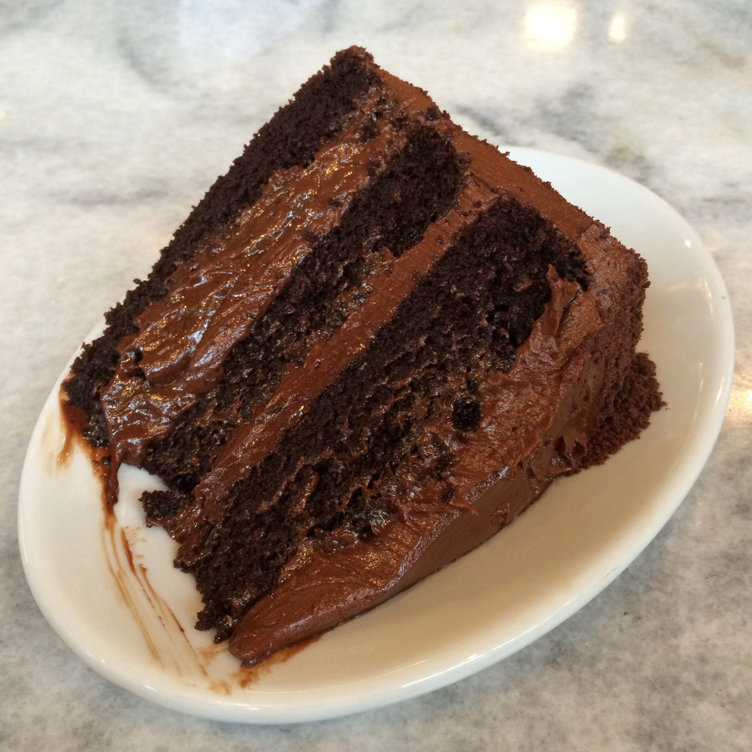 A slice of chocolate layer cake with chocolate frosting on a white plate